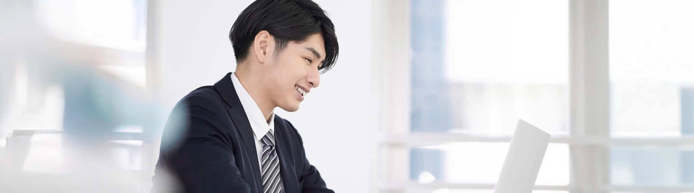 スーツ姿の若い男性がパソコン画面を見ながら微笑んでいるオフィス風景
